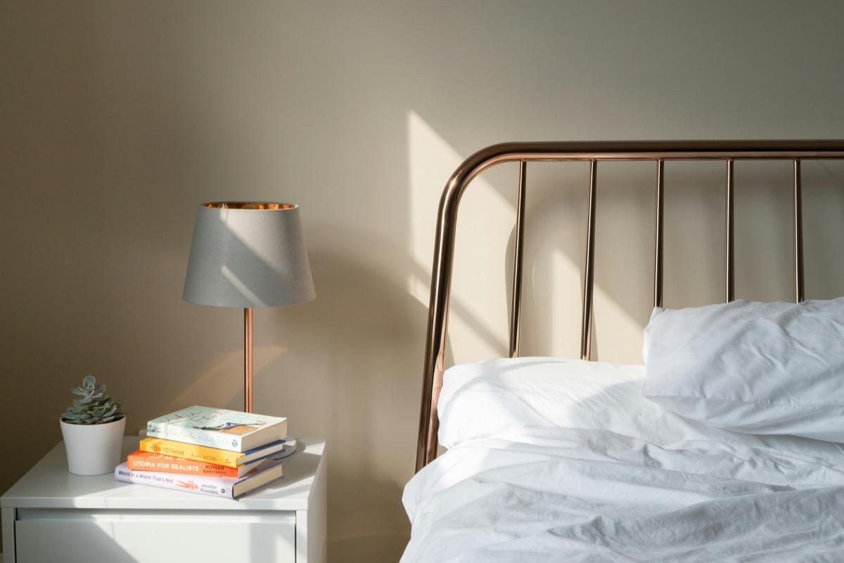 Lampe à abat-jour gris et pied cuivré sur une table de chevet blanche près d'un lit