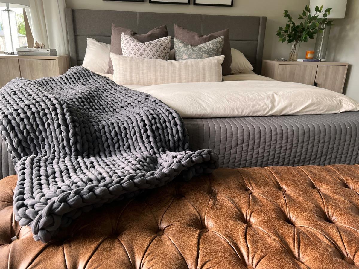 Plaid gris en grosse maille posé sur une banquette en cuir au pied d'un lit