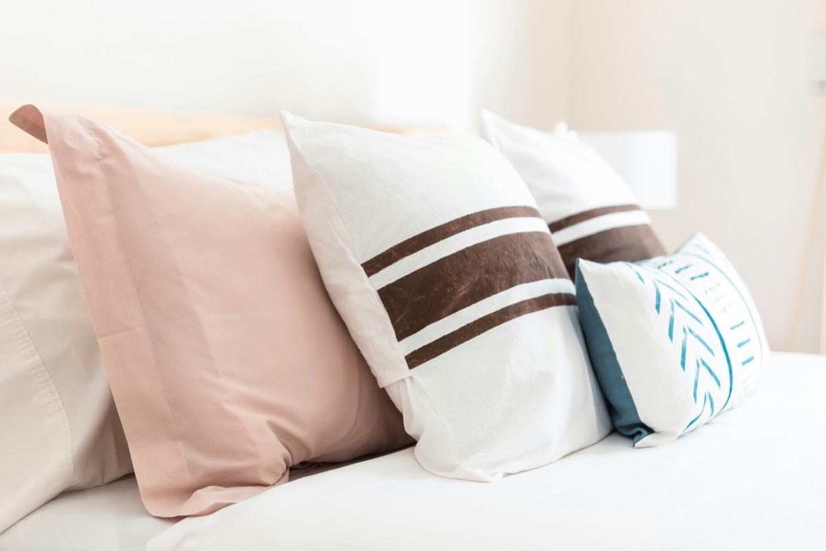 Coussins décoratifs rose poudré, rayés et à motifs disposés sur un lit blanc