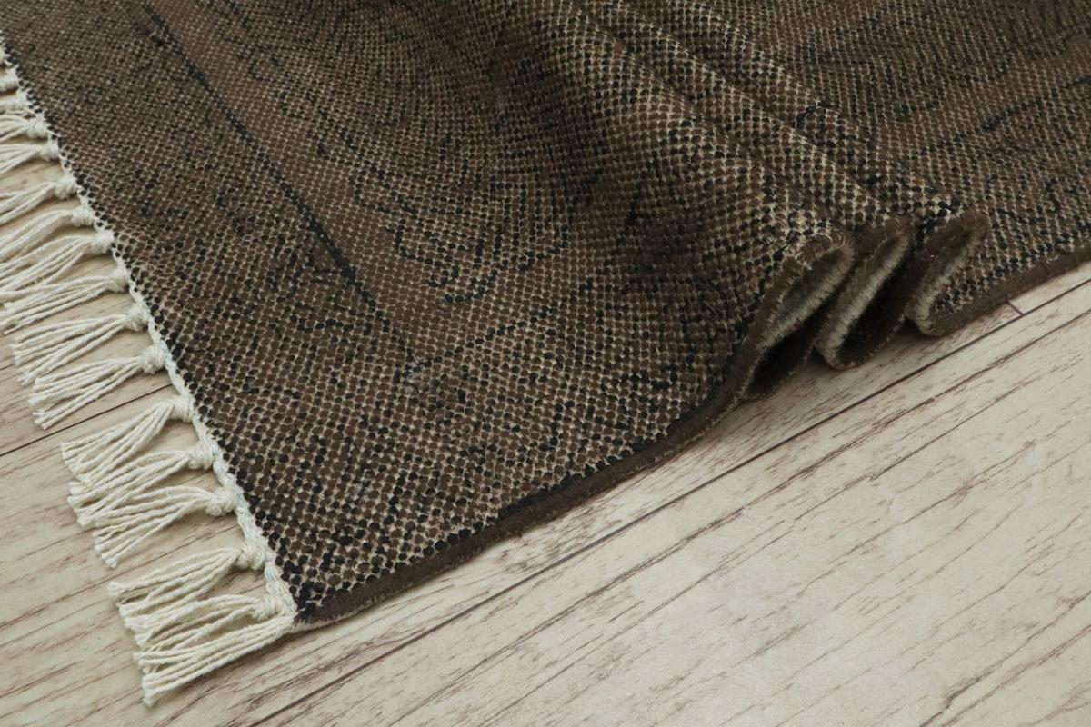 Coin d'un tapis brun à franges sur un parquet