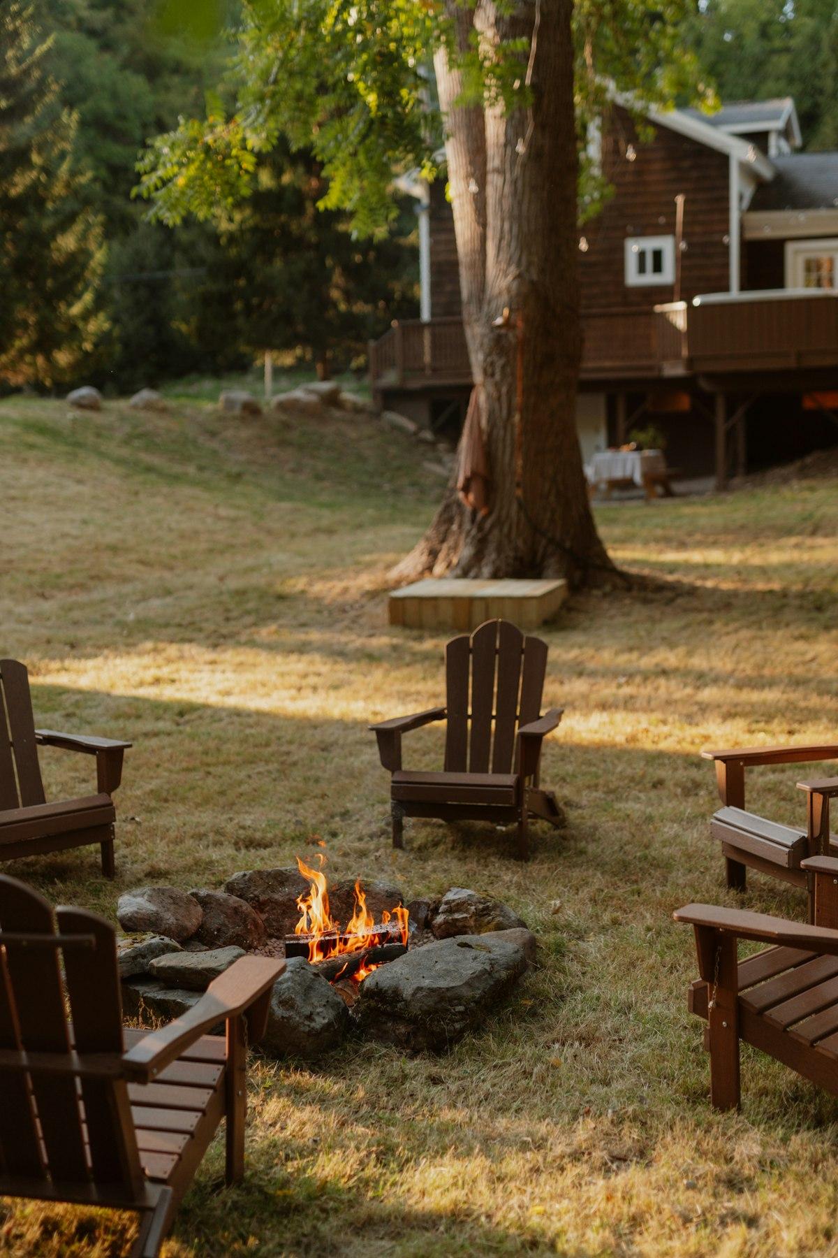 Brasero de jardin en pierre avec flammes entouré de fauteuils Adirondack à l'heure dorée