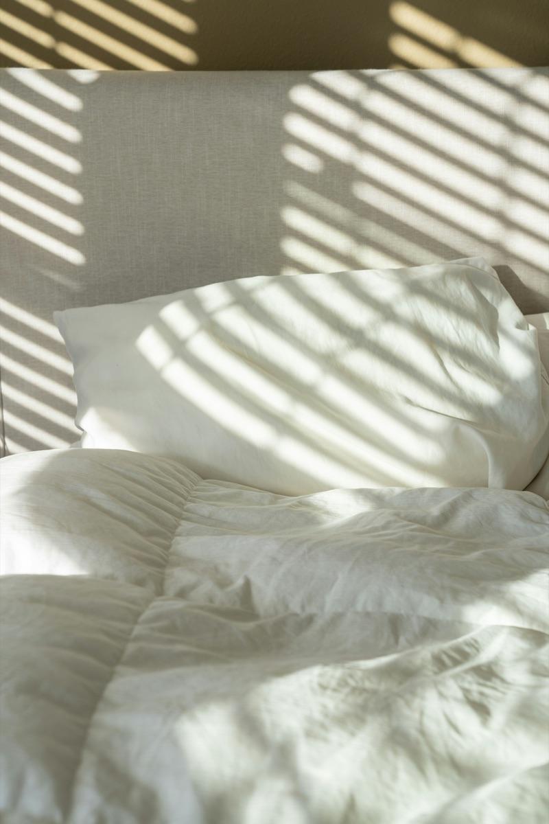 Couette et oreiller en lin lavé blanc avec des rayures de soleil chaudes sur le lit