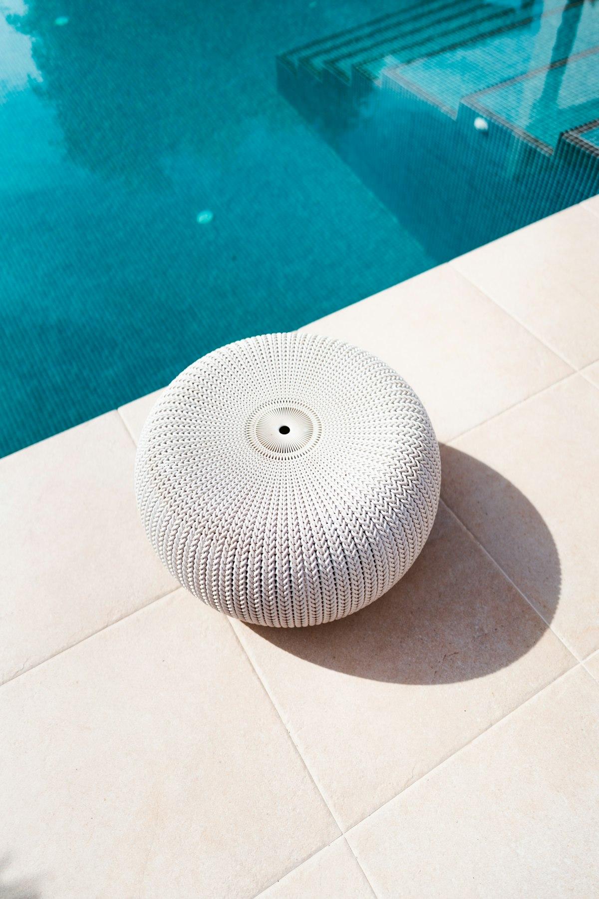 Pouf d'extérieur blanc en résine tricotée au bord d'une piscine